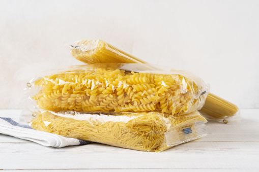 Various pasta in transparent plastic bags on a kitchen table. Grocery goods. Spaghetti, fusilli and vermicelli.