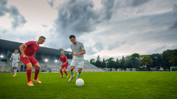 istock Professional Soccer Player Leads with a Ball, Masterfully Dribbling and Bypassing Sliding Tackles of His Opponents. Two Professional Football Teams Playing. Low Angle Shot. 1161534935
