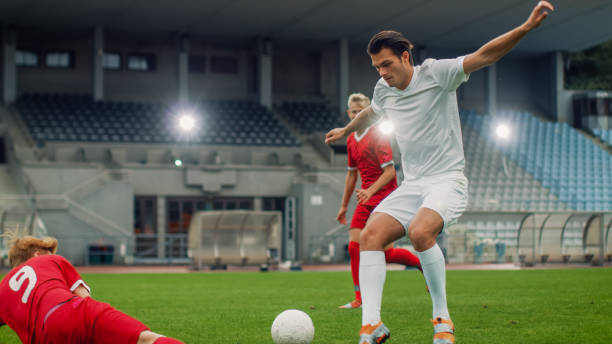 istock Professional Soccer Player Leads with a Ball, Masterfully Dribbling and Bypassing Sliding Tackles of His Opponents. Two Professional Football Teams Playing. Low Angle Shot. 1161534981
