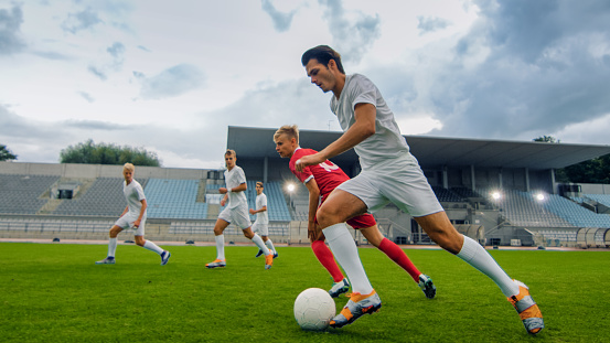 Male soccer players running and leading ball during match on sports field, side view wide shot