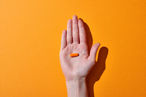 partial view of woman holding orange pill on orange background