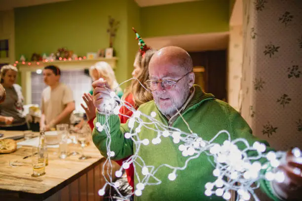A shot of a senior caucasian man trying to untangle some Christmas lights, he is struggling.