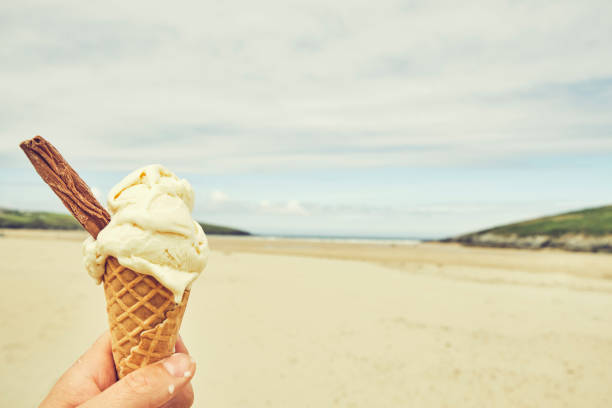 istock POV hand holding a Vanilla Ice cream cone at Crantock Beach, Newquay, Cornwallmon a June day, mild vintage film tone. 1161551524