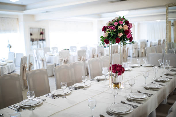 Beautiful flower decoration on tables with plates, glasses and eating utensils, in luxury banquet hall