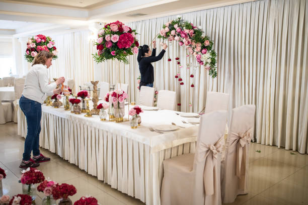 Everything is almost finished for wedding ceremony Two hard working women finishing decorating of banquet hall with blossom flowers busy restaurant tables stock pictures, royalty-free photos & images
