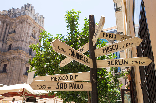Pole guidepost with multiple destination cities of the world on arrows sticks in Spanish. Places at Malaga downtown