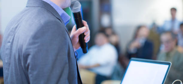 Speaker giving a talk at a corporate business conference. Audience in hall with presenter in front of presentation screen. Corporate executive giving speech during business and entrepreneur seminar. stock photo