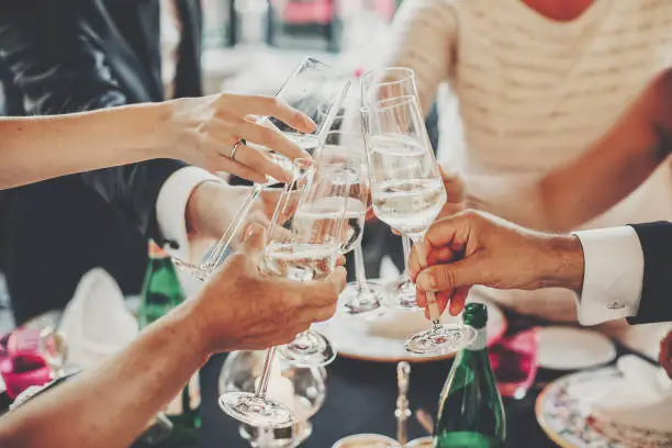 Hands toasting with champagne glasses at wedding reception outdoors in the evening. Family and friends clinking glasses and cheering with alcohol at delicious feast celebration. Christmas party