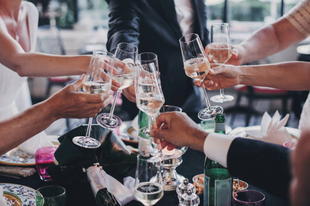 gruppe von menschen halten champagnergläser und toasten bei hochzeitsempfang im freien am abend. familie und freunde klirren gläser und jubeln mit alkohol bei leckerem fest - festmahl stock-fotos und bilder