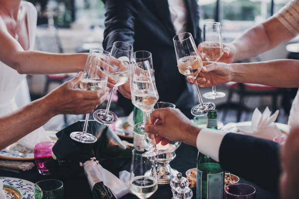 Group of people holding champagne glasses and toasting at wedding reception outdoors in the evening. Family and friends clinking glasses and cheering with alcohol at delicious feast celebration stock photo