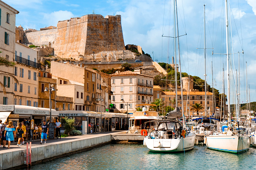 Bonifacio, France - September 19, 2018: People walking by the port of Bonifacio, in Corsica, France, with the famous citadel of the city in the background, on the top of a promontory
