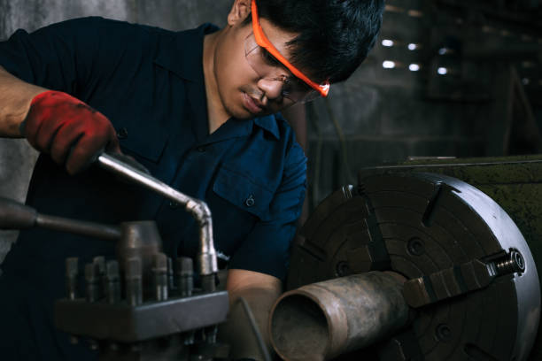 Diverse Asian manufacturing engineer using a socket hand tool to adjust industrial lathe equipment in factory workshop stock photo