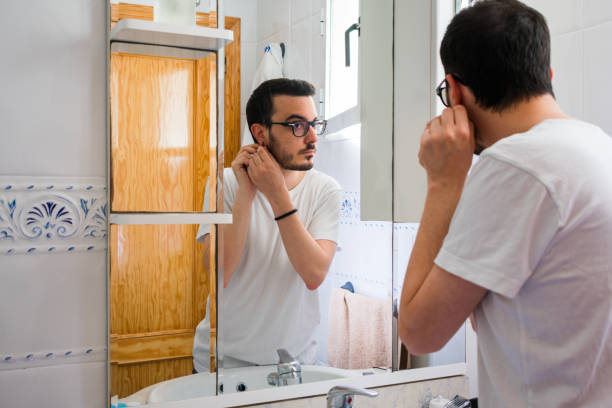 istock Man looking at himself in a mirror in the bathroom. He is getting an earring 1161582504
