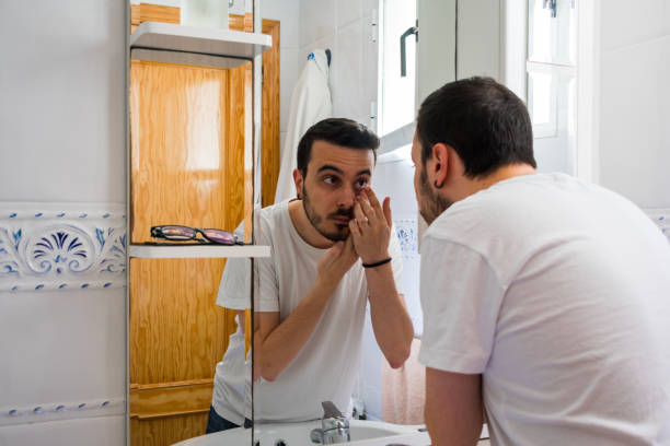 istock Man looking at himself in a mirror in the bathroom. He is putting a lens 1161582510