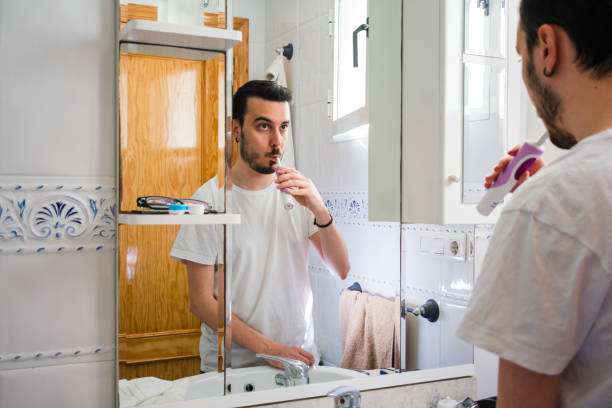 istock Man looking at himself in a mirror in the bathroom. He is brushing his teeth 1161582523