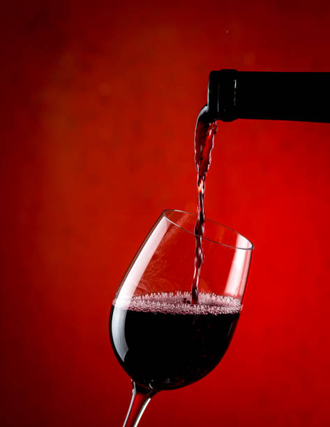 Pouring red wine into a glass, red background Pouring red wine into a glass, red background. chilean wine stock pictures, royalty-free photos & images