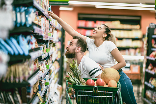 Female Stretching Above Boyfriend To Buy Groceries
