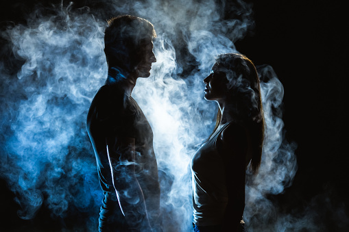 The man and woman standing in smoke on the dark background