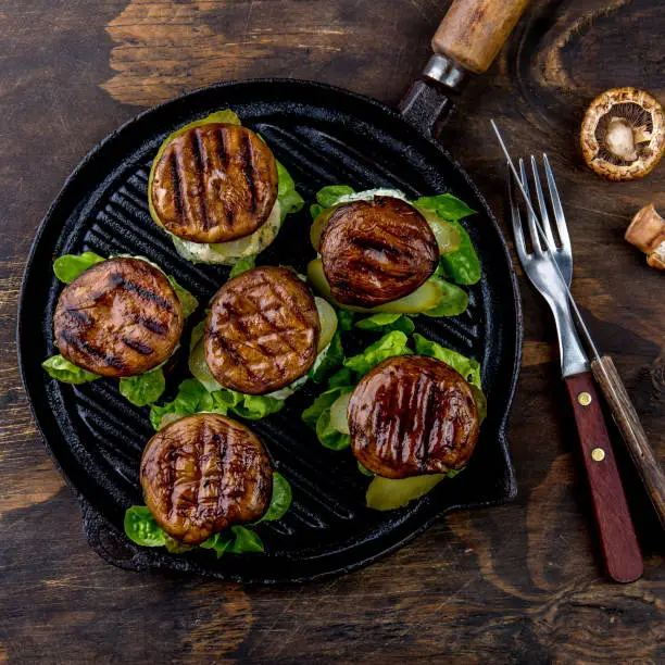Grilled portobello bun mushroom burgers on cast iron grill pan ob wooden background, top view.