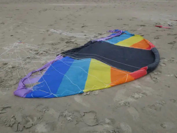 a kite in rainbowcolors with white threads laying on the beach of Velsen Netherlands
