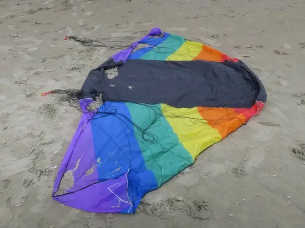 a kite in rainbowcolors with black threads laying on the beach of Velsen Netherlands
