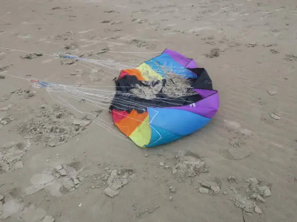 a crinkled kite in rainbowcolors with white threads laying on the beach of Velsen Netherlands
