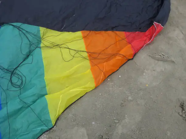 a detail of a kite in rainbowcolors with black threads laying on the beach of Velsen Netherlands