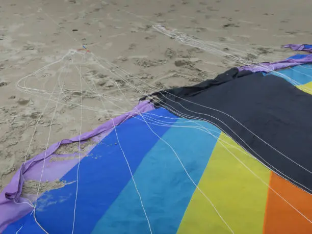 a part of a kite in rainbowcolors with black threads laying on the beach of Velsen Netherlands