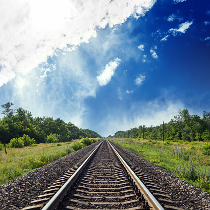 railroad in green landscape to horizon in blue cloudy sky