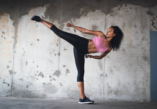 Balance is everything Full length shot of a young sportswoman kicking up her leg in the air while exercising inside a parking lot kickboxing stock pictures, royalty-free photos & images