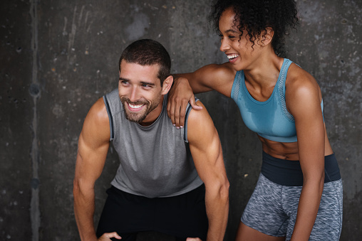 Shot of a sporty young couple resting against a wall while exercising inside a parking lot