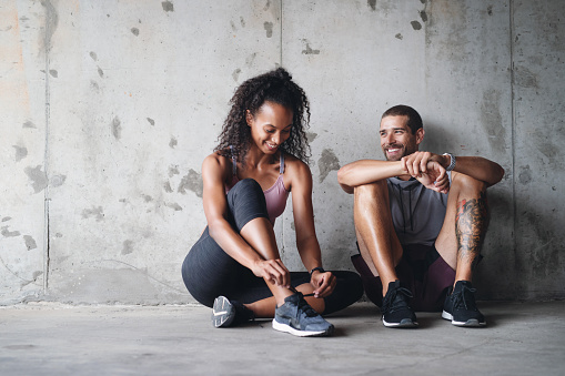 Full length shot of a sporty young couple sitting down and resting against a wall