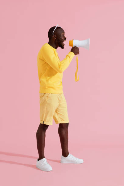 istock Attention! Black man shouting in megaphone on pink background 1161597369