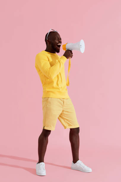istock Attention! Black man shouting in megaphone on pink background 1161597400