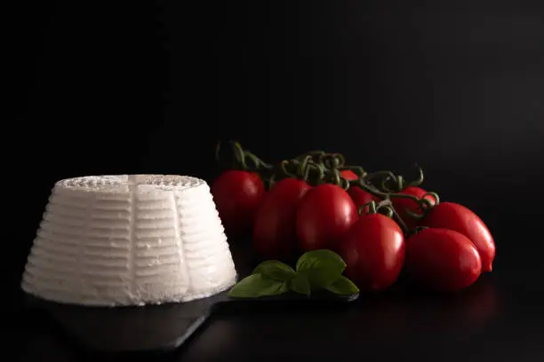 Front view view of fresh ricotta cheese with basil and cherry tomatoes on black plate italian food concept. Isolate on black background. Still life. Flat lay food.