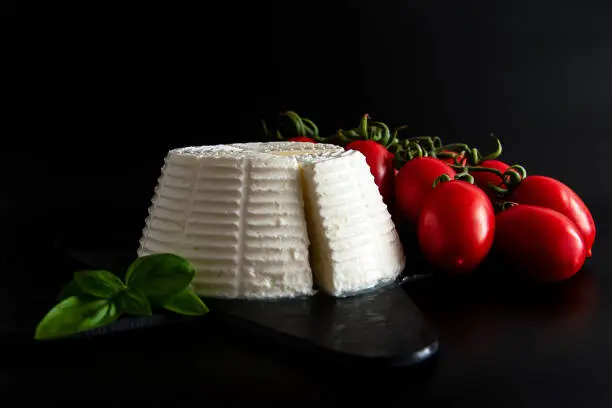 Front view view of fresh ricotta cheese with basil and cherry tomatoes on black plate italian food concept. Isolate on black background. Still life. Flat lay food.