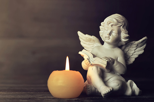 Angel and white candle on dark background. Guardian angel reading a book