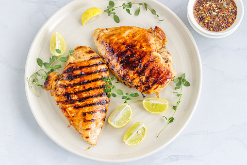 Grilled Chicken Breast on a White Plate with Lemon and Fresh Oregano.