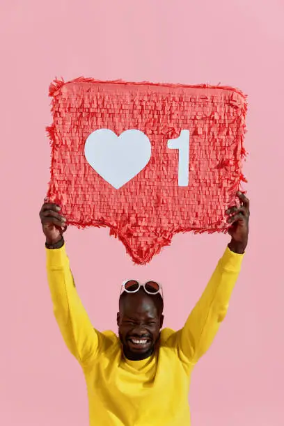 Photo of Like. Happy black man holding like heart icon pinata on pink