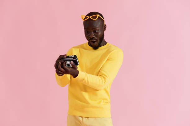 istock Surprised man looking at photos on camera on pink background 1161602481