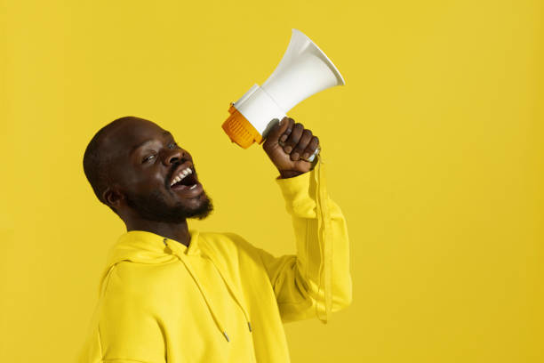 istock Attention! Black man shouting in megaphone on yellow background 1161602869