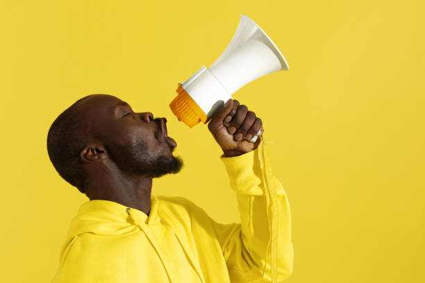 istock Attention! Black man shouting in megaphone on yellow background 1161602905