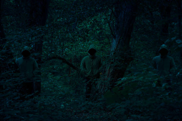 istock Three dark male figures in a hoodies standing between trees with mysterious light coming behind them 1161604214