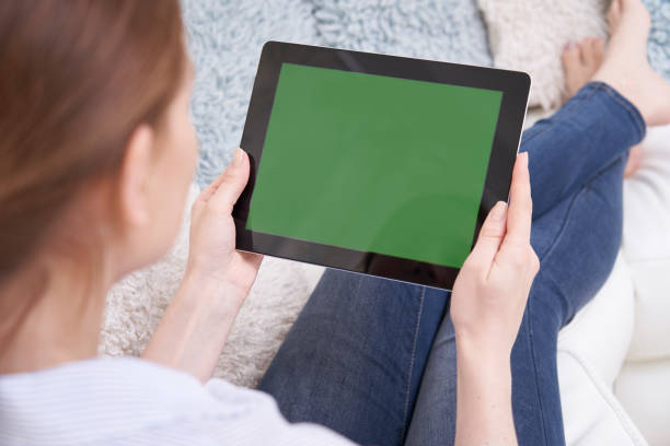 vista sulle spalle della donna sdraiata sul divano utilizzando tablet digitale a schermo verde a casa - ipad television digital tablet connection foto e immagini stock