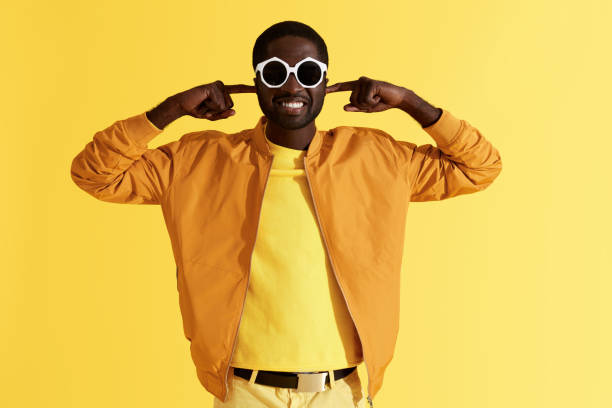 istock Man in sunglasses closing ears with hands on yellow background 1161608249