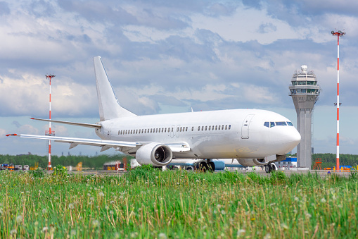 Passenger aircraft in the foreground green grass on the steering track at the airport on the background of the atc tower controllers