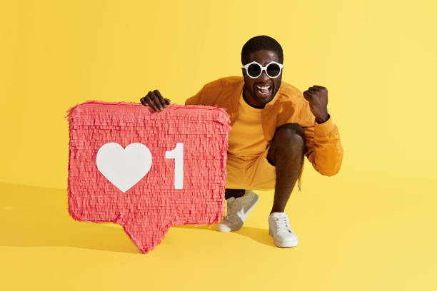 istock Smiling man with like icon, heart pinata on yellow background 1161609506