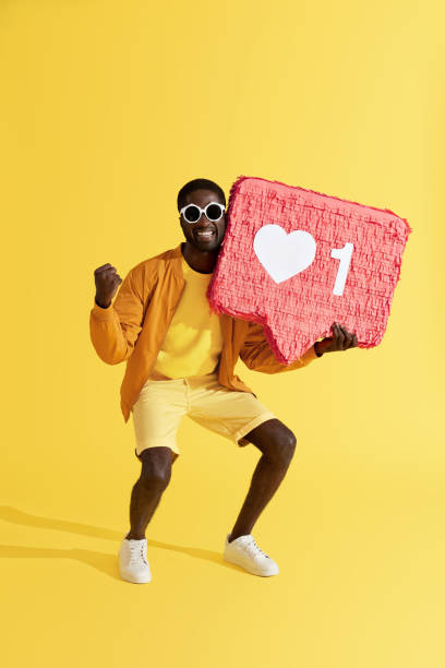 istock Smiling man with like icon, heart pinata on yellow background 1161609571