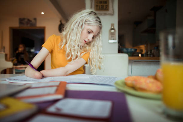 Working Hard Doing Homework A close-up shot of a young teenage amputated girl doing her homework at the dining table. 12 13 years pre adolescent child female blond hair stock pictures, royalty-free photos & images