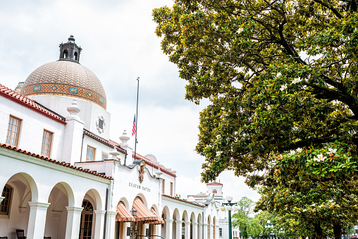 Hot Springs, USA - June 4, 2019: Historical Quapaw Baths Spa bath house with American flag and dome by many magnolia southern trees in city